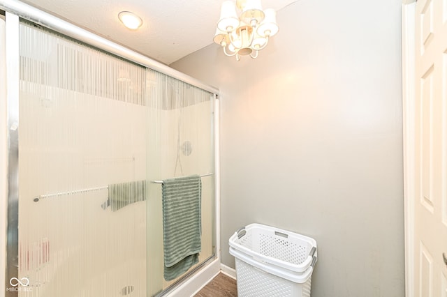 bathroom featuring hardwood / wood-style flooring, an enclosed shower, a textured ceiling, and a notable chandelier