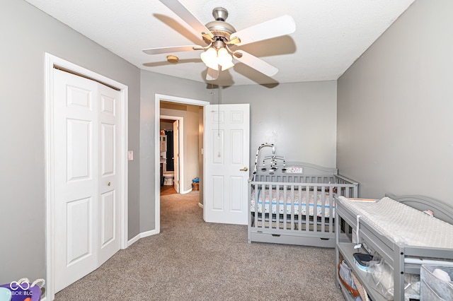 bedroom with a crib, ceiling fan, carpet flooring, a textured ceiling, and a closet