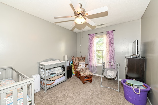 carpeted bedroom featuring ceiling fan, a textured ceiling, and a crib