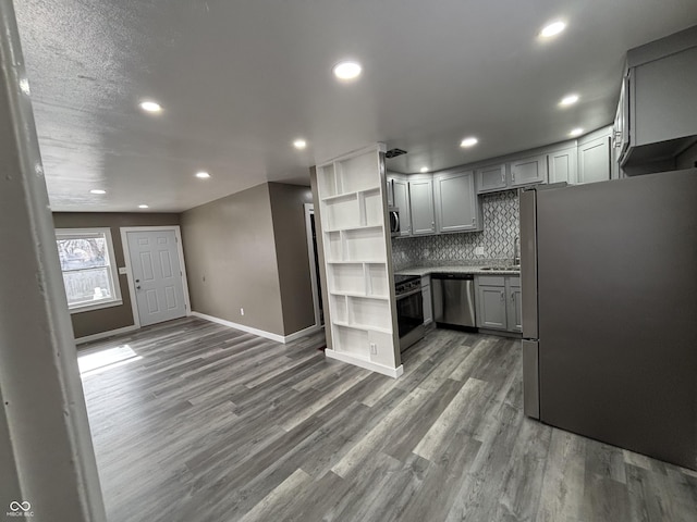 kitchen with dark wood-type flooring, gray cabinets, stainless steel appliances, and decorative backsplash