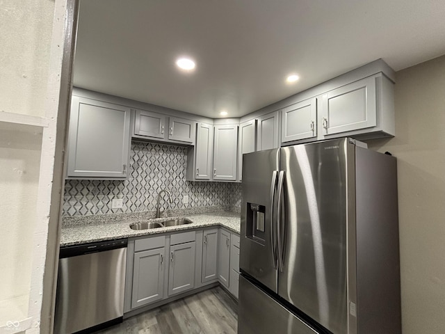 kitchen with sink, gray cabinets, backsplash, stainless steel appliances, and light stone counters