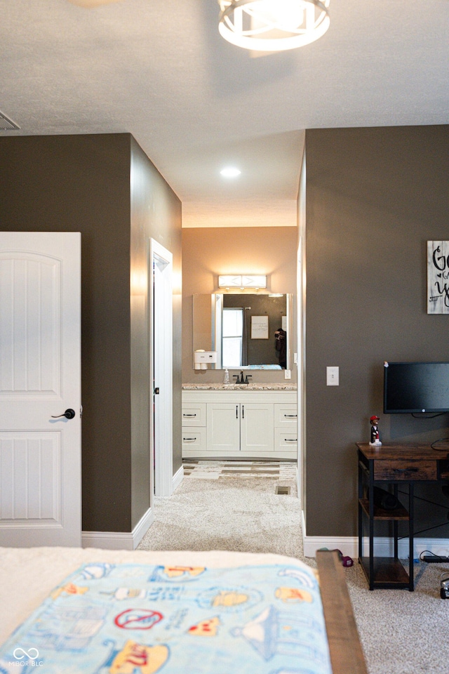 bedroom with ensuite bathroom, sink, and light colored carpet