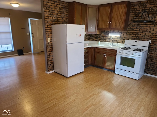 kitchen with brick wall, sink, white appliances, and light wood-type flooring