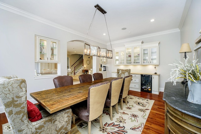 dining space with bar, an inviting chandelier, ornamental molding, dark hardwood / wood-style floors, and beverage cooler