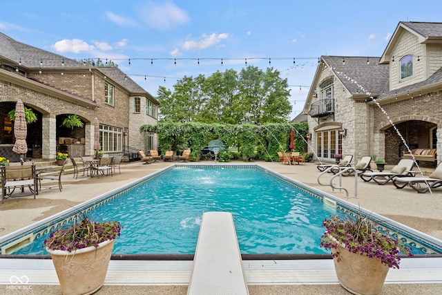 view of swimming pool featuring an outdoor brick fireplace, a diving board, a patio, and pool water feature