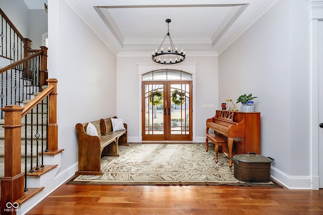 entryway with hardwood / wood-style floors, a raised ceiling, crown molding, an inviting chandelier, and french doors