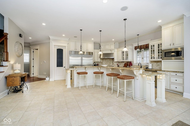 kitchen with a kitchen bar, light stone counters, built in appliances, decorative light fixtures, and wall chimney range hood