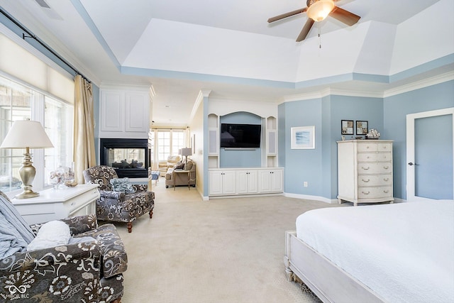 bedroom with crown molding, ceiling fan, a multi sided fireplace, a raised ceiling, and light colored carpet