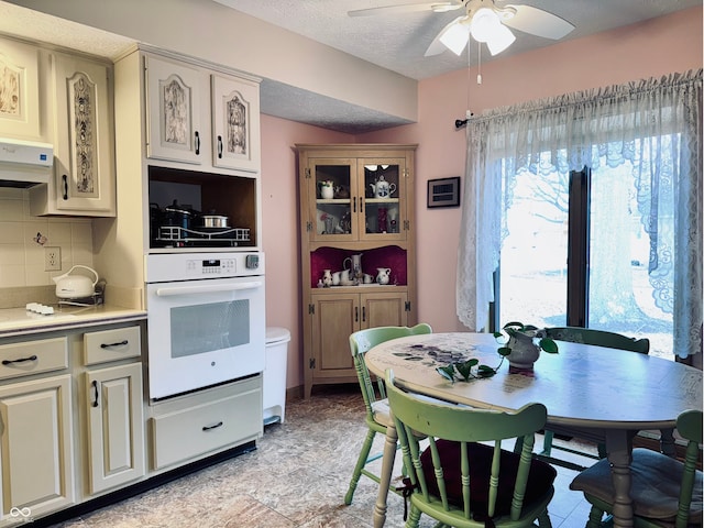 kitchen featuring tasteful backsplash, oven, a textured ceiling, and cream cabinetry