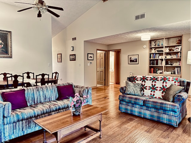 living room with hardwood / wood-style flooring, ceiling fan, high vaulted ceiling, and a textured ceiling