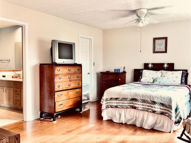 bedroom featuring ceiling fan, ensuite bath, light hardwood / wood-style flooring, and a textured ceiling