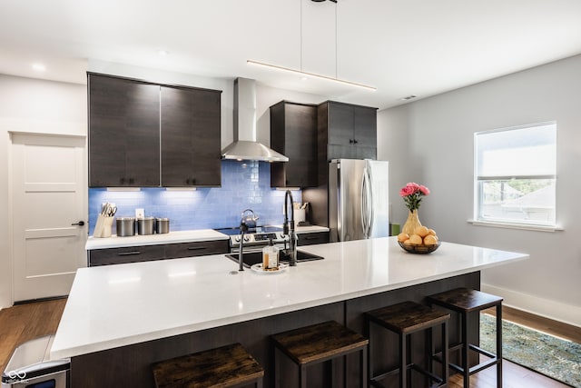 kitchen featuring a kitchen bar, a center island with sink, stainless steel refrigerator, and wall chimney exhaust hood