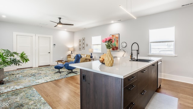 kitchen with dishwasher, sink, a kitchen island with sink, dark brown cabinets, and light hardwood / wood-style flooring