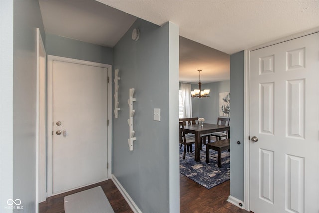 entryway with baseboards, a textured ceiling, an inviting chandelier, and dark wood-style flooring