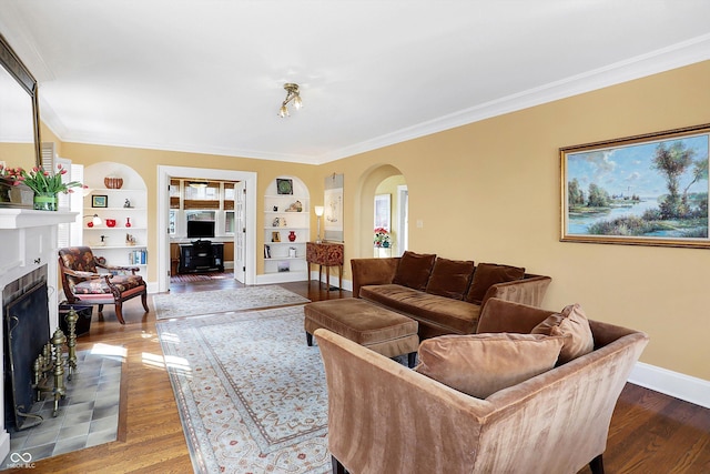 living area featuring arched walkways, a tile fireplace, wood finished floors, crown molding, and built in shelves