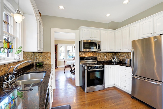 kitchen with a sink, white cabinets, appliances with stainless steel finishes, dark stone countertops, and dark wood finished floors