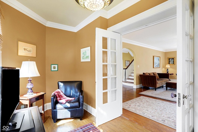 sitting room with ornamental molding, arched walkways, baseboards, and wood finished floors