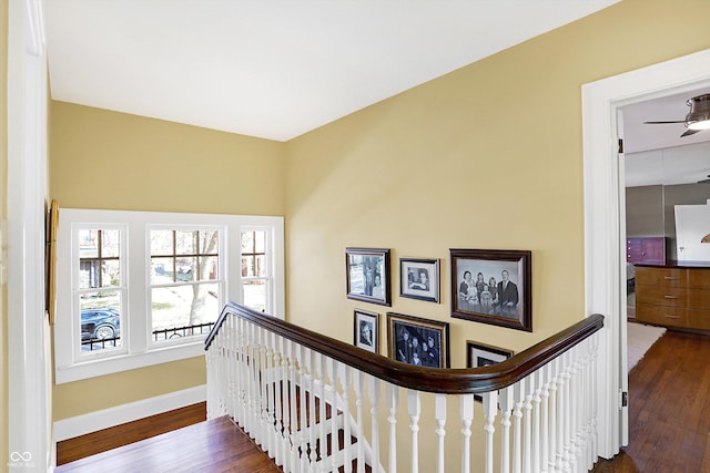 hall featuring dark wood-style flooring, an upstairs landing, and baseboards