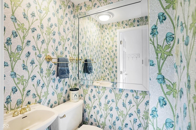 half bathroom featuring toilet, wallpapered walls, and a sink