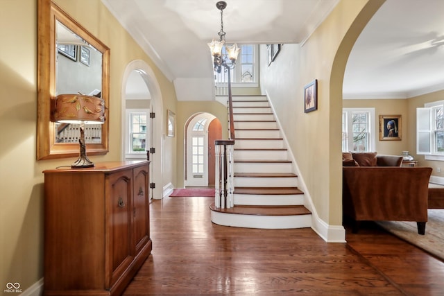 entrance foyer with arched walkways, ornamental molding, and dark wood-style floors