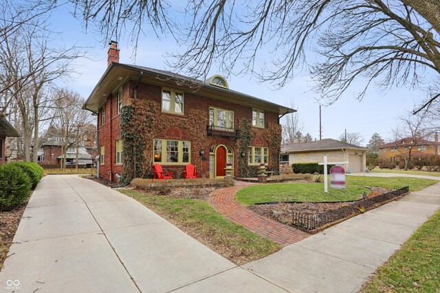 colonial-style house with driveway, brick siding, a chimney, and a front lawn