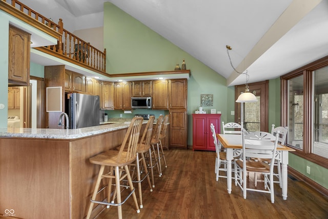 kitchen featuring pendant lighting, dark wood-type flooring, a breakfast bar area, stainless steel appliances, and light stone countertops