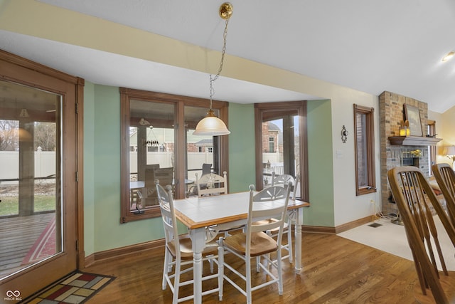 dining space featuring vaulted ceiling, a brick fireplace, and dark wood-type flooring