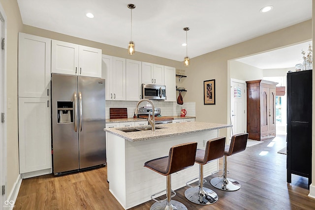 kitchen with pendant lighting, white cabinetry, stainless steel appliances, light stone counters, and a center island with sink