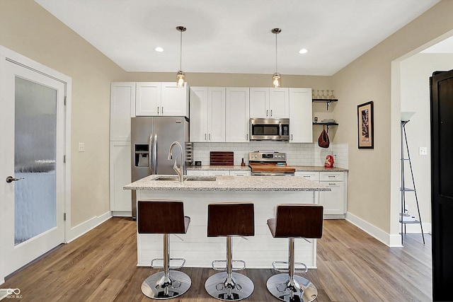 kitchen with a kitchen island with sink, pendant lighting, white cabinets, and appliances with stainless steel finishes