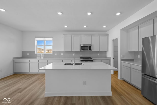 kitchen featuring sink, tasteful backsplash, a center island with sink, stainless steel appliances, and light hardwood / wood-style floors