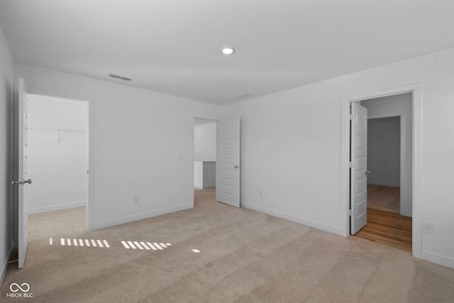 unfurnished bedroom with a walk in closet, light colored carpet, and a closet