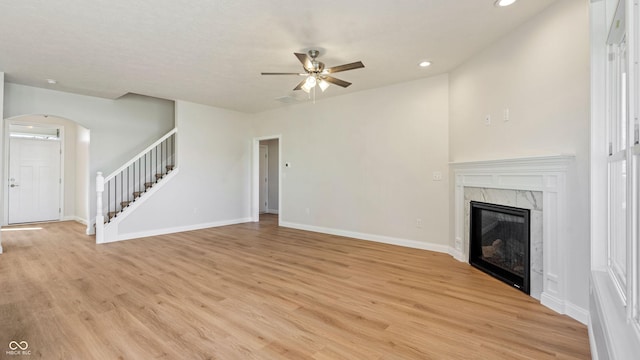 unfurnished living room with a premium fireplace, ceiling fan, and light wood-type flooring