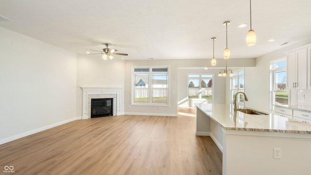 kitchen featuring sink, light stone counters, light hardwood / wood-style flooring, hanging light fixtures, and white cabinets