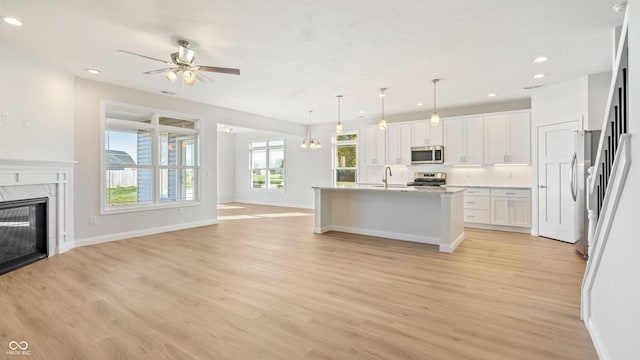 kitchen with white cabinetry, hanging light fixtures, a center island with sink, stainless steel appliances, and a premium fireplace