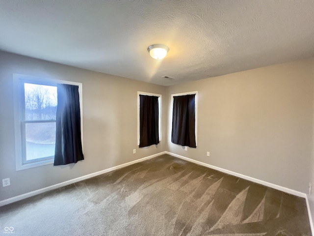 spare room with a textured ceiling and dark colored carpet