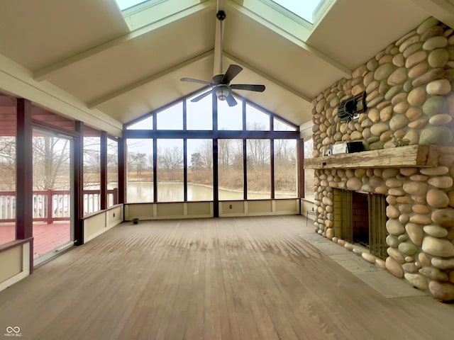 unfurnished sunroom featuring a water view, a healthy amount of sunlight, a stone fireplace, and lofted ceiling with skylight