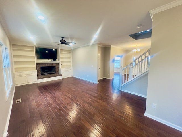 unfurnished living room featuring crown molding, dark hardwood / wood-style floors, built in features, a fireplace, and ceiling fan with notable chandelier