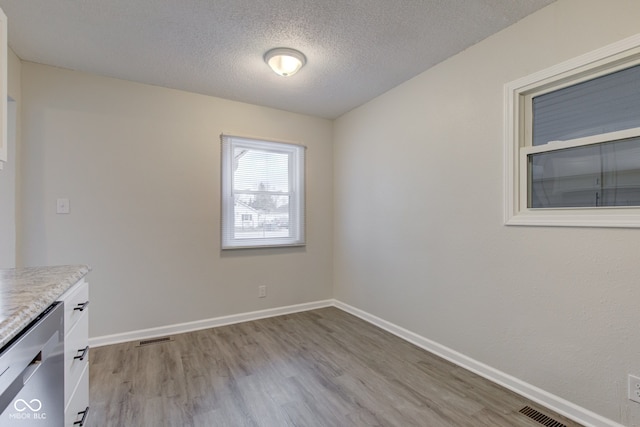 unfurnished dining area featuring a textured ceiling and light wood-type flooring