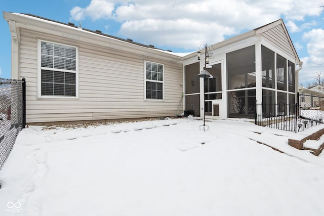 snow covered back of property featuring a sunroom and fence