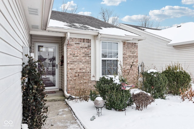 snow covered property entrance featuring a shingled roof and brick siding