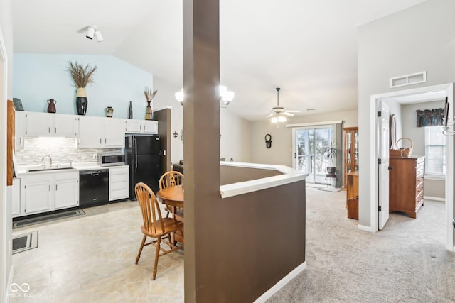 kitchen with lofted ceiling, black appliances, white cabinetry, and a sink