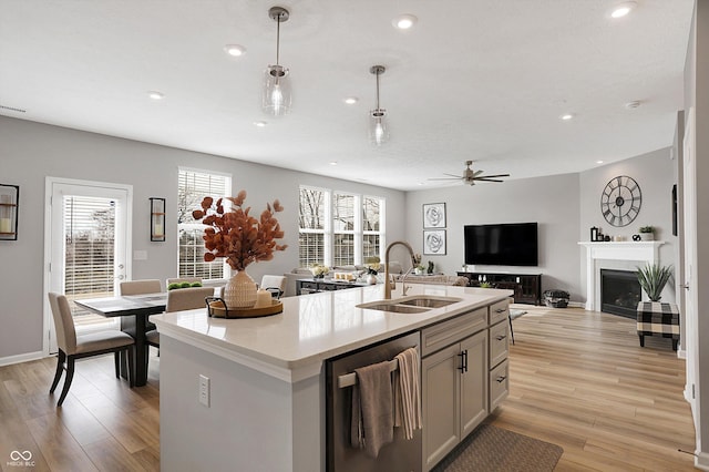 kitchen with pendant lighting, sink, light hardwood / wood-style floors, an island with sink, and stainless steel dishwasher