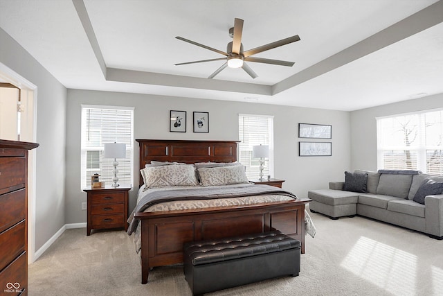 carpeted bedroom with a raised ceiling, ceiling fan, and multiple windows