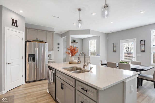 kitchen featuring appliances with stainless steel finishes, an island with sink, sink, gray cabinetry, and hanging light fixtures