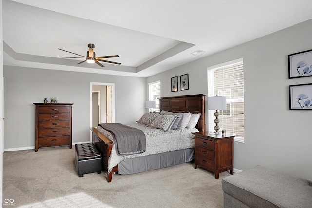 bedroom with ceiling fan, light colored carpet, and a tray ceiling