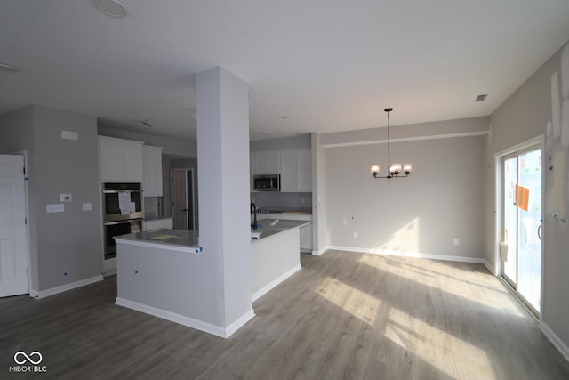 kitchen featuring white cabinetry, stainless steel appliances, a notable chandelier, and wood finished floors