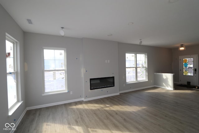 unfurnished living room featuring a glass covered fireplace, visible vents, baseboards, and wood finished floors