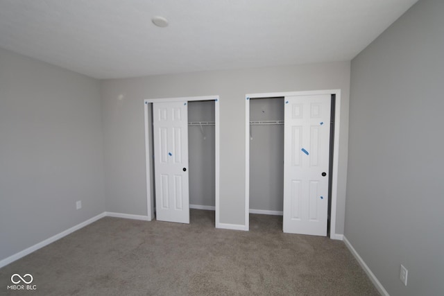 unfurnished bedroom featuring carpet flooring, baseboards, and two closets