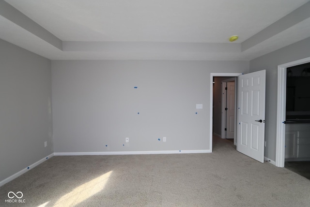 unfurnished bedroom with carpet floors, baseboards, and a raised ceiling