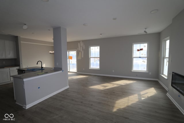 interior space featuring dark wood finished floors, open floor plan, a sink, and baseboards